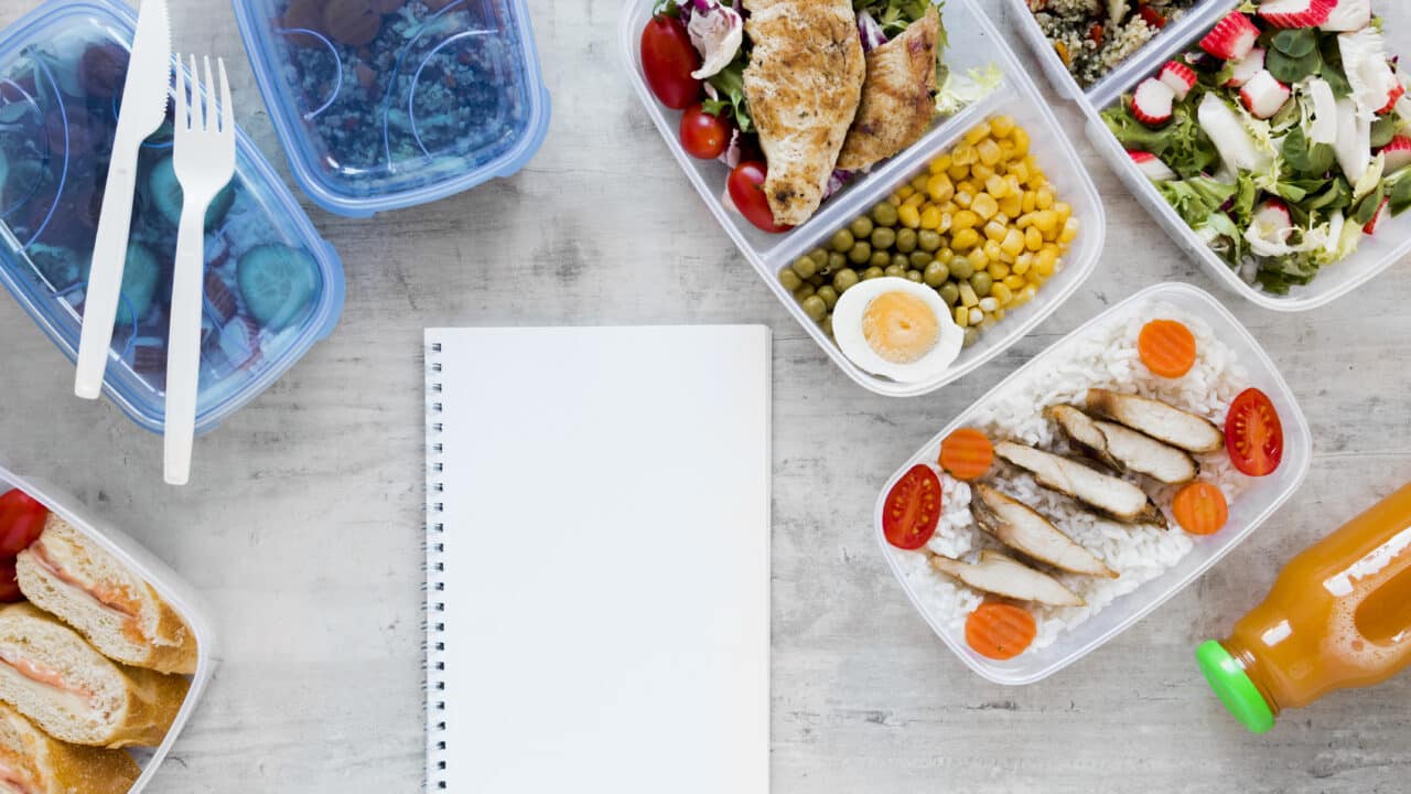 Meal prep containers arranged next to a planning notebook, top view flat lay