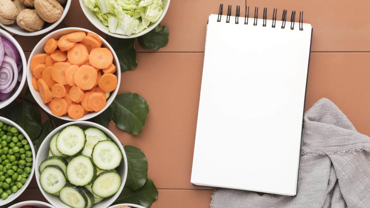 Bowls of sliced vegetables next to a notepad, weekly meal planning flat lay