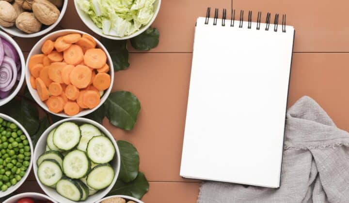 Bowls of sliced vegetables next to a notepad, weekly meal planning flat lay