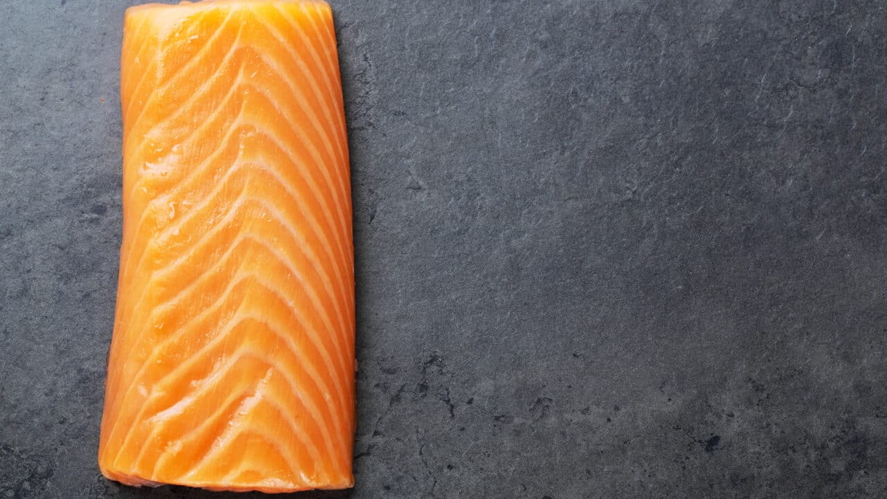 Raw salmon fillet on a dark stone surface, showing the fresh color and texture to check before refrigerating