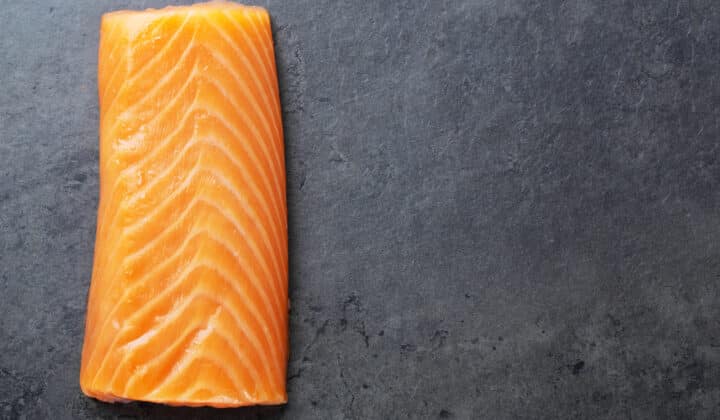 Raw salmon fillet on a dark stone surface, showing the fresh color and texture to check before refrigerating