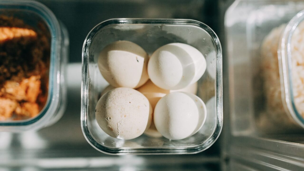 Peeled and unpeeled hard-boiled eggs stored in a container in the fridge