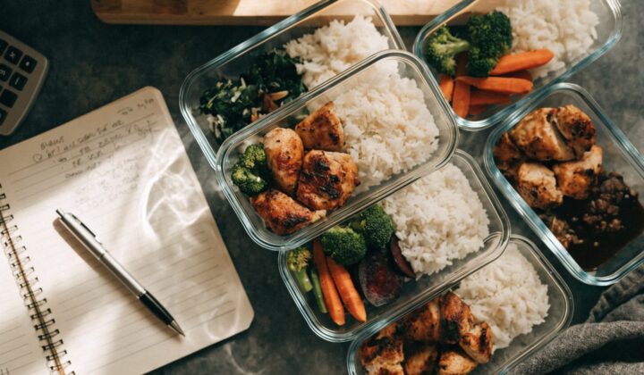 Meal prep containers with portioned food next to a notebook and calculator for tracking cost per meal