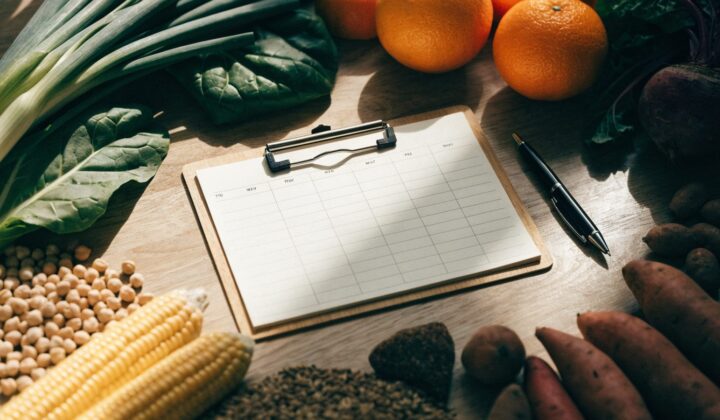 Weekly meal plan on a clipboard surrounded by fresh food, overhead flat lay view