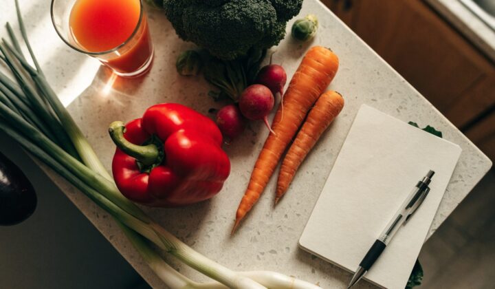 Blank weekly menu template notepad with a pen next to fresh vegetables and a glass of juice