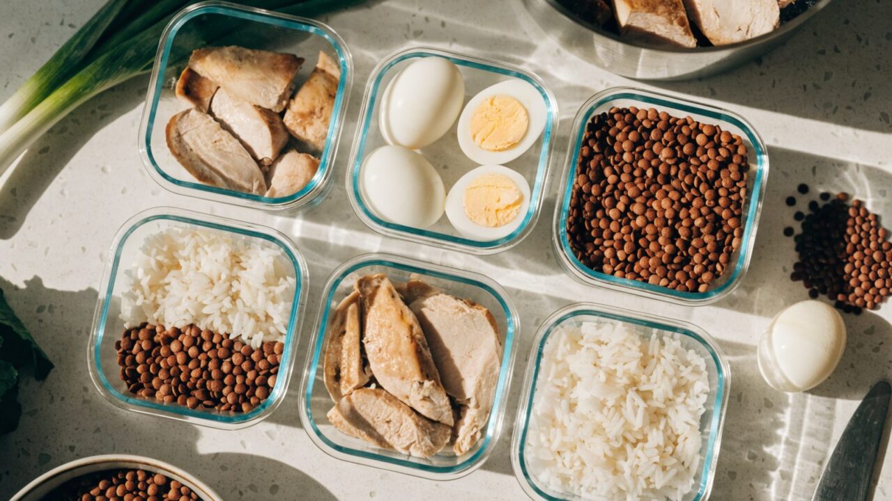 Weekly protein meal prep with chicken, eggs, lentils and rice in containers, top-down view