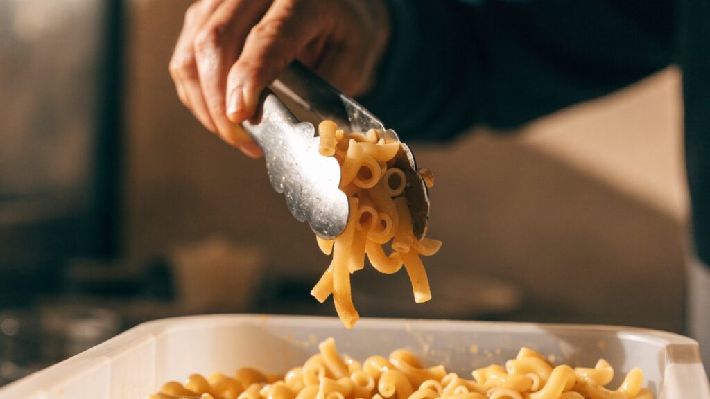 Cooked pasta being portioned into a shallow storage container