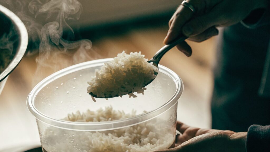 Cooked white rice being scooped into a storage container