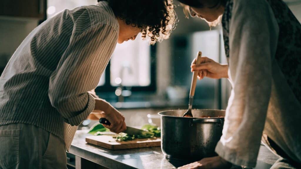 Two people cooking together in a kitchen, one chopping vegetables