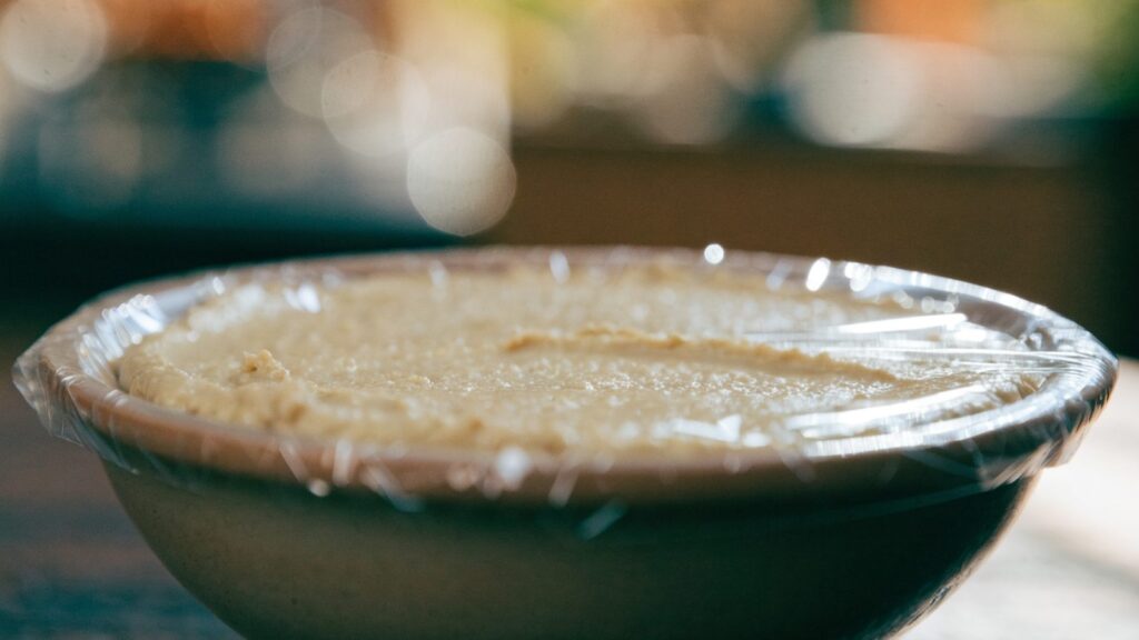 A bowl of hummus with plastic wrap pressed directly onto its surface