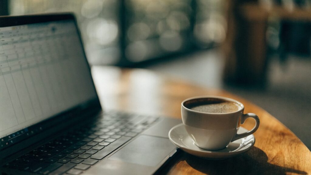 A laptop showing a spreadsheet-style meal planner next to a cup of coffee