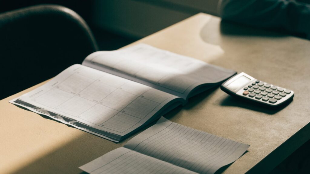 A printed weekly planner, grocery list and calculator laid out on a desk