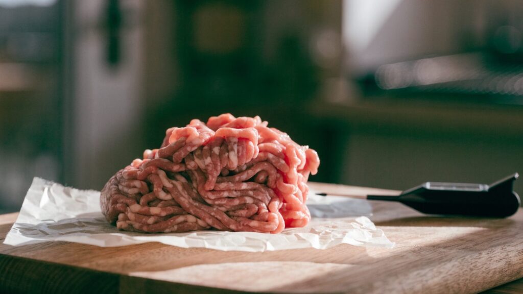 Raw ground beef on butcher paper next to a digital food thermometer