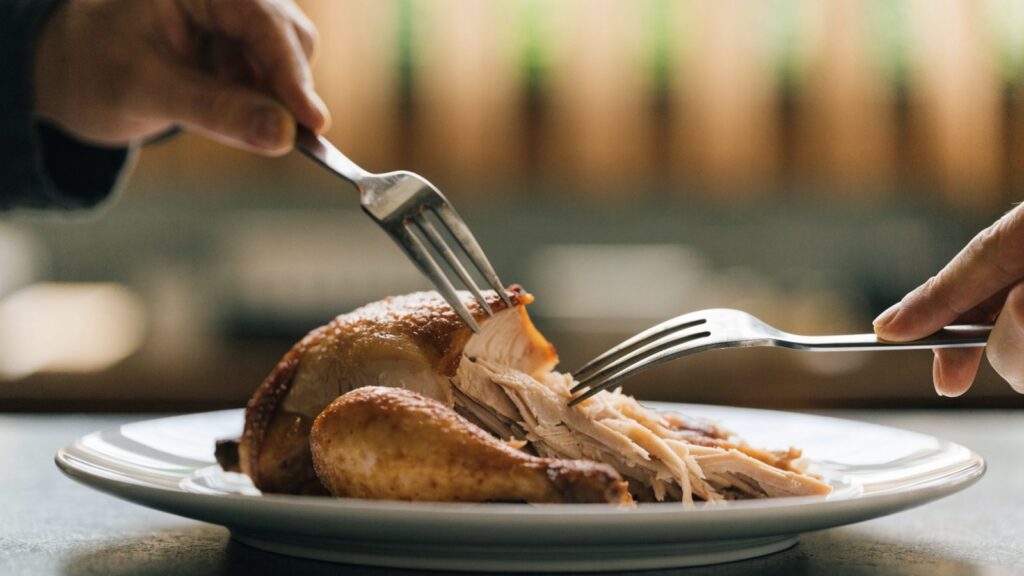 A rotisserie chicken on a plate being shredded with two forks