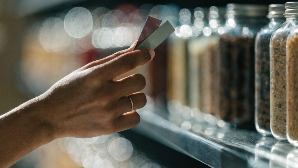 A hand comparing price tags between two products on a supermarket shelf
