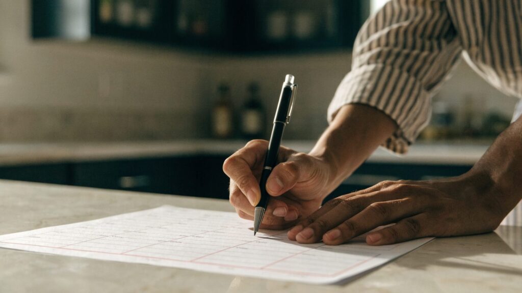 Hands writing on a printed weekly meal planner grid on a kitchen counter