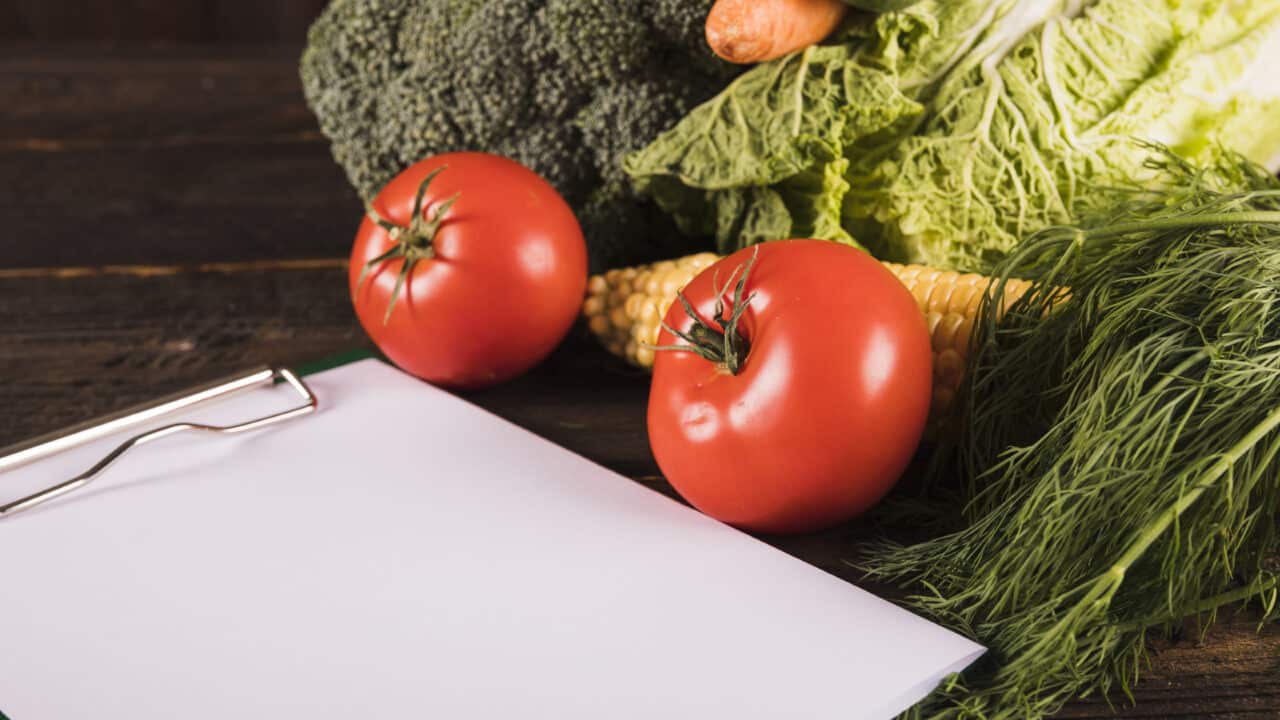 A blank clipboard surrounded by fresh raw vegetables, ready for a budget grocery list