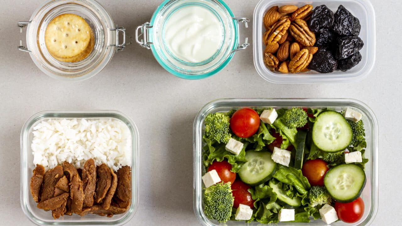 Raciones individuales de arroz, proteína, ensalada, frutos secos y yogur repartidas en botes pequeños sobre una encimera.