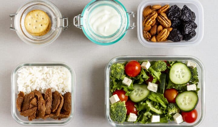Raciones individuales de arroz, proteína, ensalada, frutos secos y yogur repartidas en botes pequeños sobre una encimera.