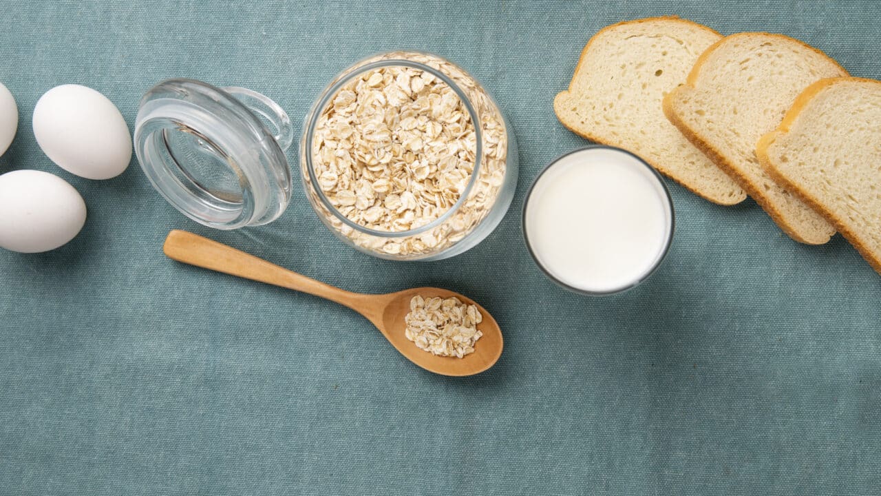 Bocal de flocons d'avoine, œufs, lait et tranches de pain sur fond bleu, ingrédients d'un petit déjeuner protéiné