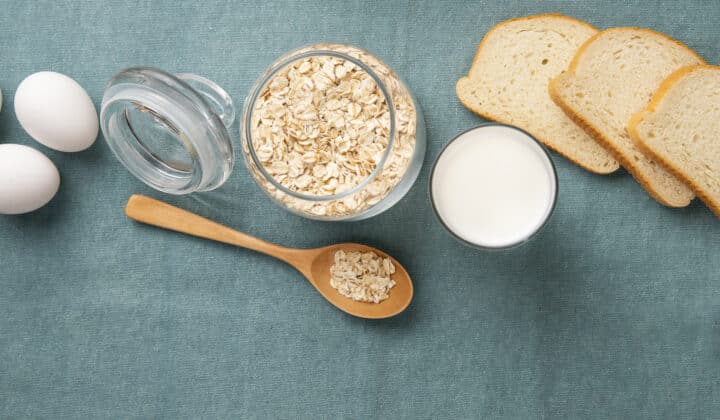 Bocal de flocons d'avoine, œufs, lait et tranches de pain sur fond bleu, ingrédients d'un petit déjeuner protéiné